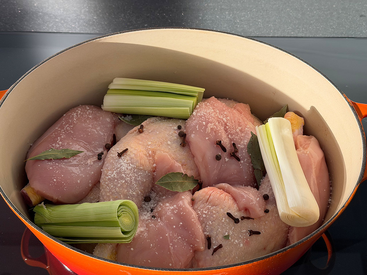 Ein großer Bräter ist gefüllt mit Hühnerschenkeln und Hühnerbrüsten zusammen mit Porrestangen und Gewürzen für Hühnerbrühe