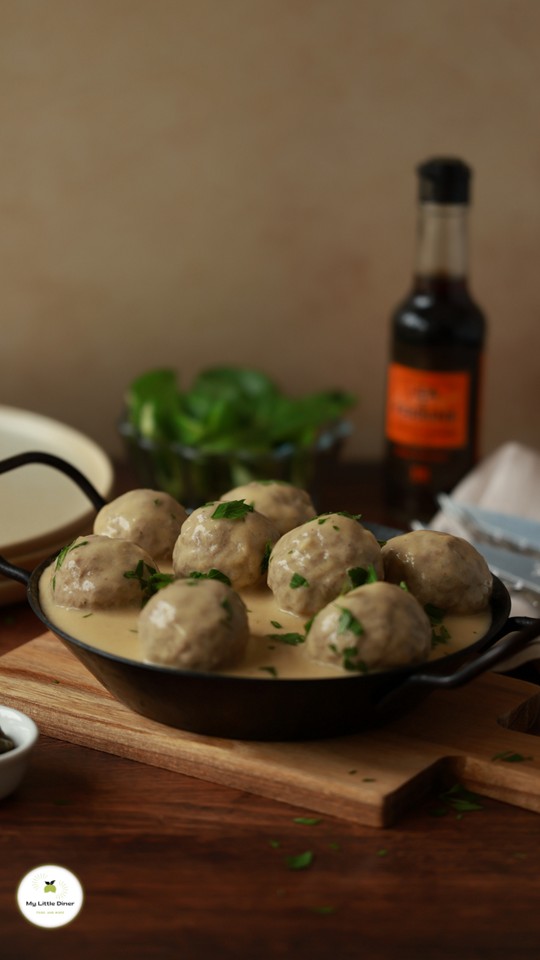 Bild zeigt Königsberger Klopse mit heller cremiger Sauce in einer dunklen Eisenpfanne mit frischer grüner Petersilie bestreut