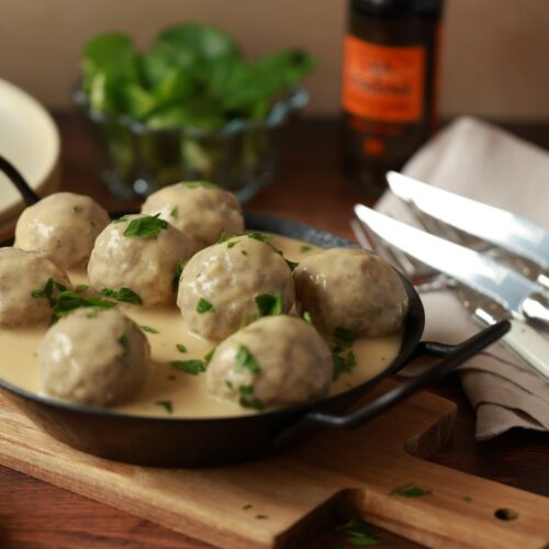 Bild zeigt Königsberger Klopse mit heller cremiger Sauce in dunkler Eisenpfanne- Titelbild Rezept