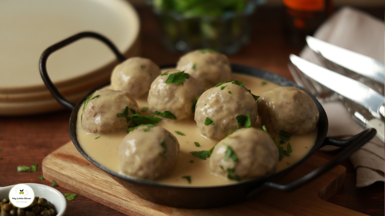 Bild zeigt Königsberger Klopse mit heller Sauce in dunkler Eisenpfanne als Rezept Titelbild