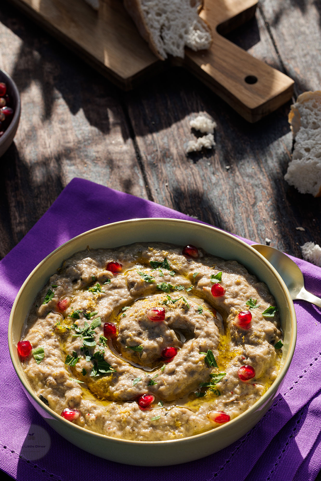 Baba Ganoush in einer Schale auf Holztisch unter Schatten von Bäumen