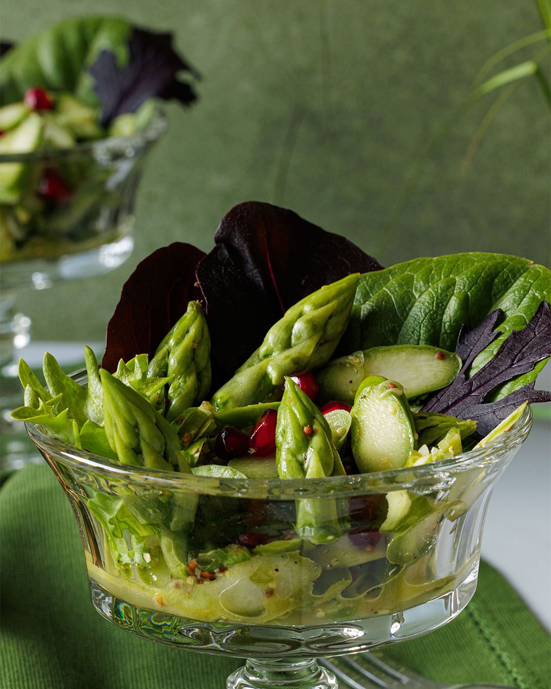 grüne Spargelstücke in einem Glas auf bunten Salatblättern mit Granatapfelkernen und Dressing